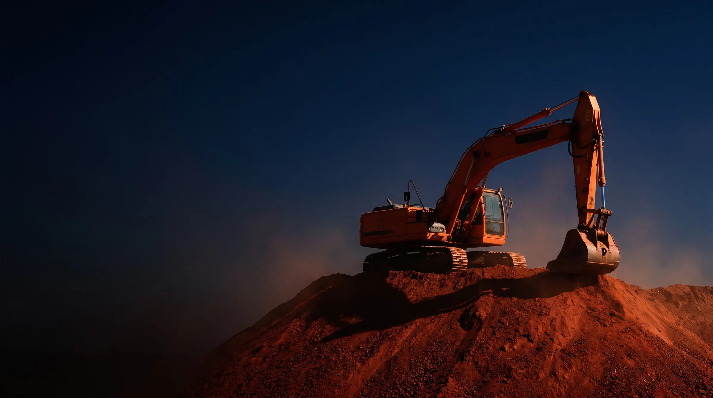 Escavadeira sobre monte de terra vermelha ao entardecer